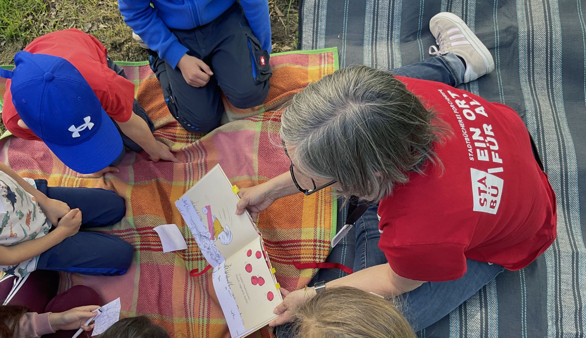 Kindergruppe auf der Wiese bekommen eine Geschichte vorgelesen